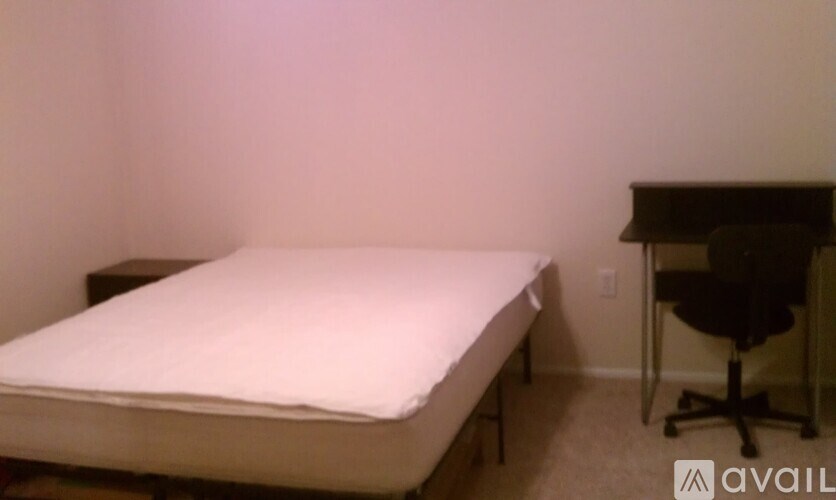 A bed with a white mattress is in a room with a desk and chair.