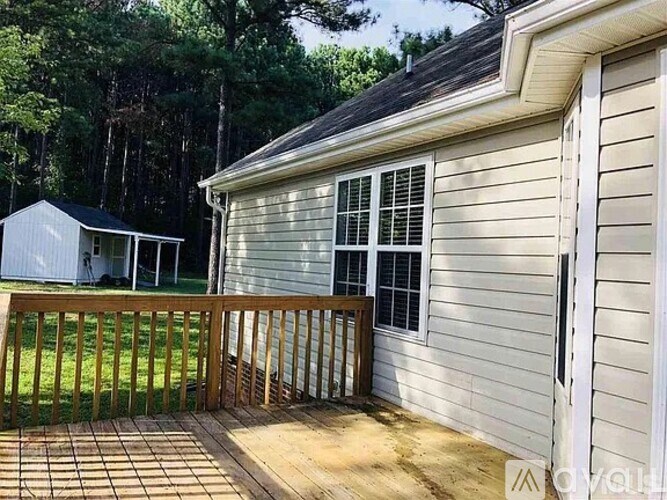 A small house with a deck and a white shed in the background.