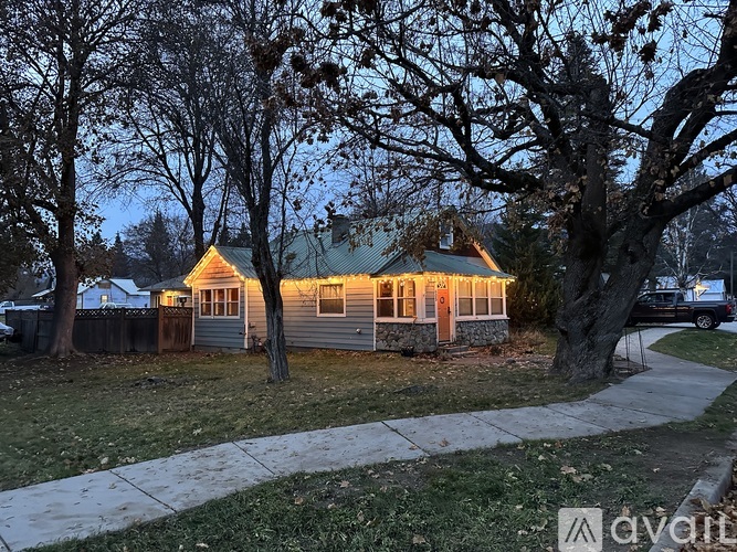 A house with a lit up front porch surrounded by trees.