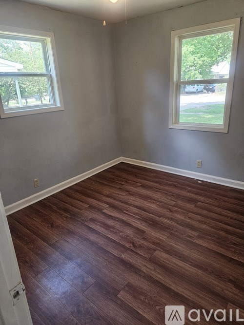 A room with wooden flooring and two windows.