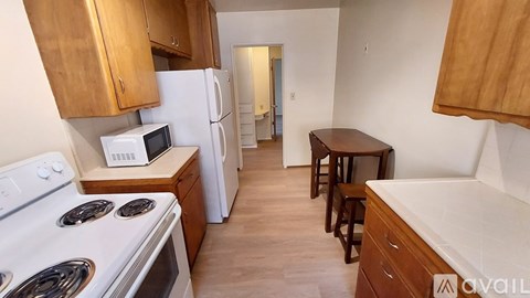 A kitchen with a white stove top oven, a microwave, a refrigerator, a washing machine, and a table with chairs.