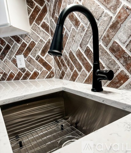A kitchen sink with a black faucet and a brick wall in the background.