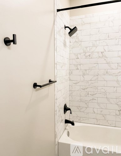 A white tiled shower area with a black shower head and faucet.