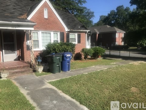 A house with a red brick exterior and a green trash can in front.