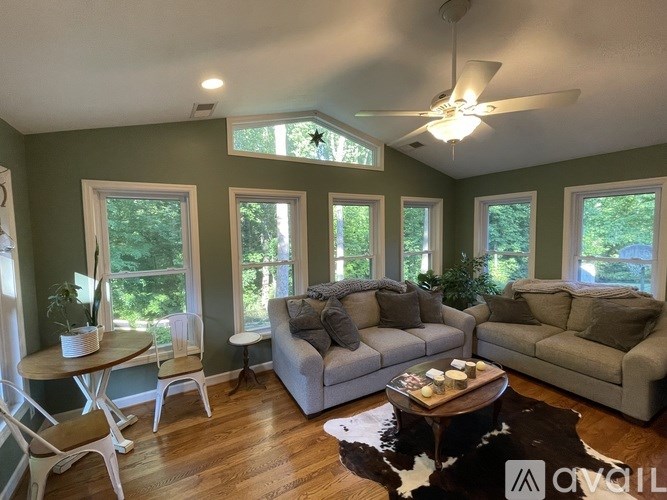 A living room with a grey couch, a white chair, a wooden coffee table and a ceiling fan.