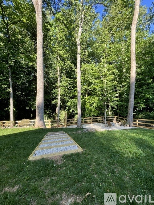 A pathway with blue flowers in the middle of a grassy area surrounded by trees.