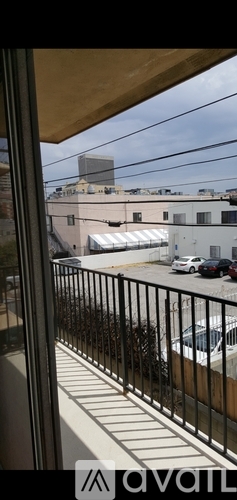 A balcony with a metal railing overlooks a parking lot and buildings.