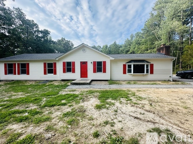 A white house with red shutters stands in a grassy field.