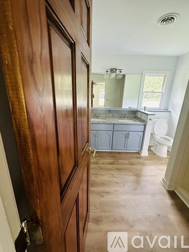 A wooden door opens to a bathroom with a tub, toilet, and sink.