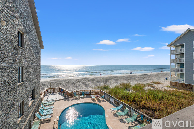 A pool with lounge chairs is surrounded by a stone building and a beach.