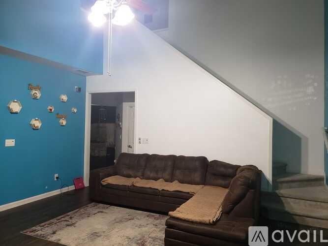 A brown couch sits in a room with a blue wall and a staircase.