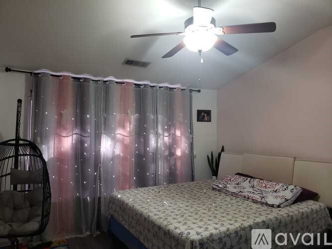 A bedroom with a bed, a hanging chair, and a ceiling fan.