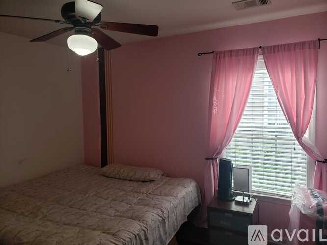 A bedroom with a bed, a ceiling fan, and a window with pink curtains.