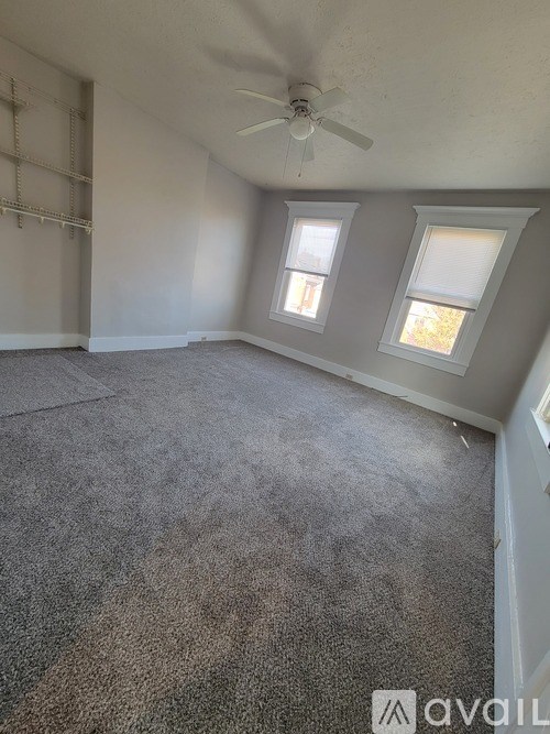 A room with a carpeted floor, a ceiling fan, and two windows.