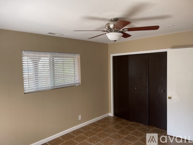 A room with a ceiling fan, a window with blinds, and a brown door.