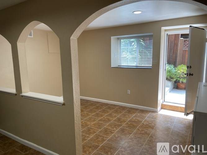 A room with beige walls and a tiled floor with an arched doorway leading to a patio.