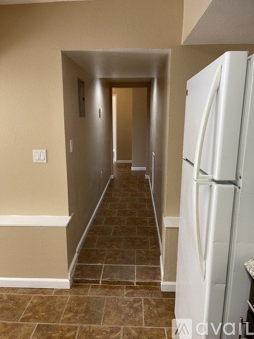 A white refrigerator stands in a narrow hallway with tiled floors.