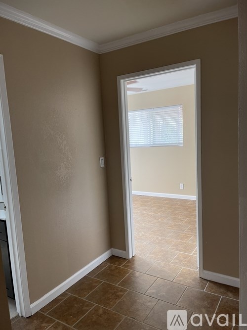 A room with beige walls and a tiled floor leading to a hallway.