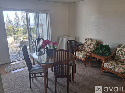 A living room with a glass table and chairs, a sofa, and a view of trees outside the window.