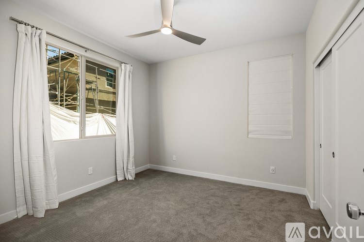 A room with a fan, carpet, and a window with curtains.