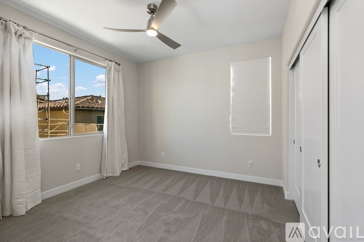 A room with a fan, carpeted floor, and a window with curtains.