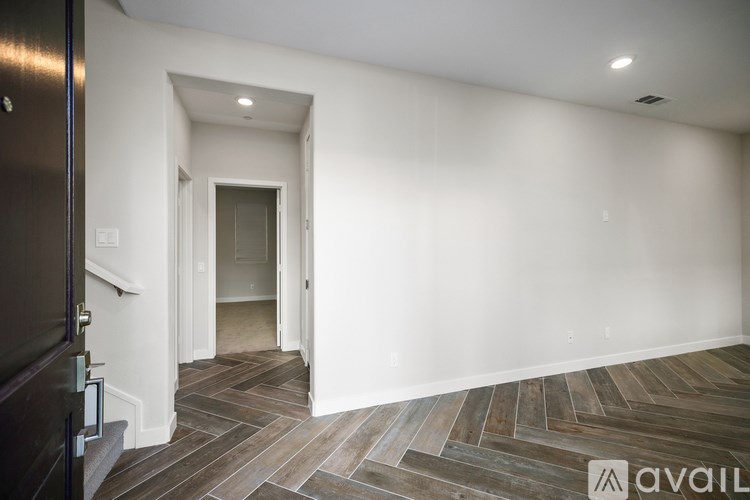 A room with a wooden floor and a white wall with a doorway leading to another room.