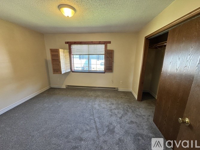 A room with a carpeted floor, a window with blinds, and a door leading to another room.