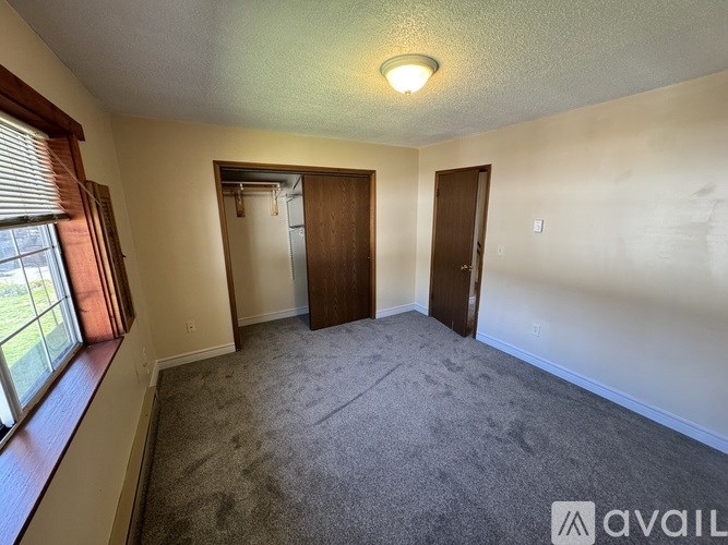 A carpeted room with a window and two doors.