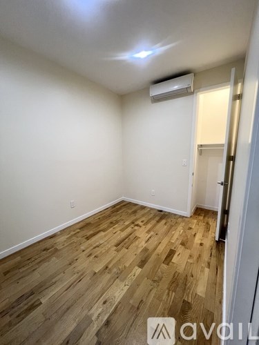 A room with wooden flooring and a white wall with a door on the right.