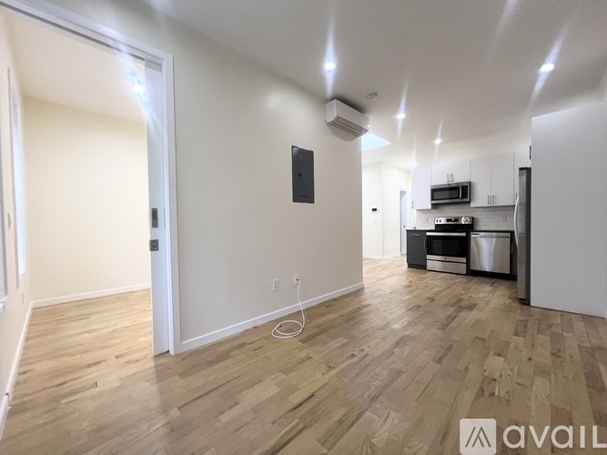 A spacious room with wooden flooring and a white wall with a black box on it.