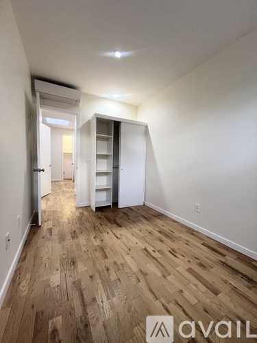 A room with wooden flooring and white walls, with a doorway leading to another room.