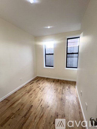 A room with wooden flooring and two windows.