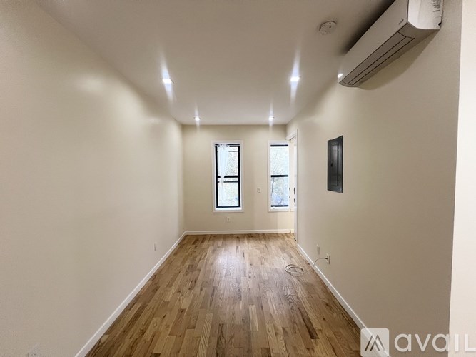 A spacious room with wooden floors and two windows.