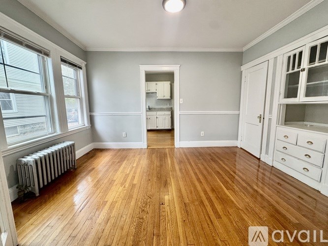 A room with wooden floors and white walls, with a window on the left and a cabinet on the right.
