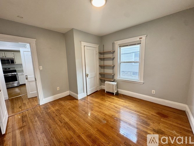 A room with wooden floors and white walls, with a window and a radiator.