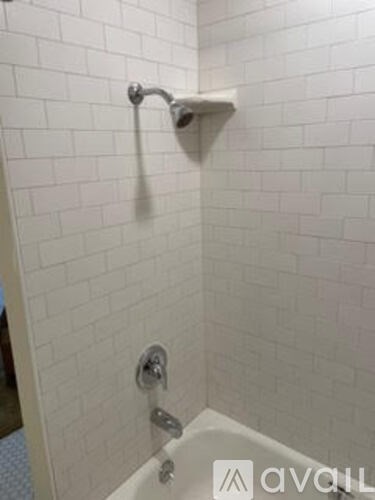 A white tiled bathroom with a white tub and shower head.