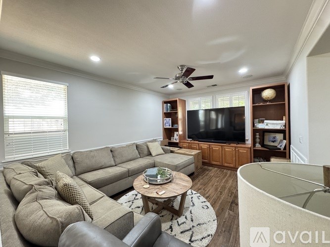 A living room with a grey sofa, a wooden coffee table, a television, and a ceiling fan.
