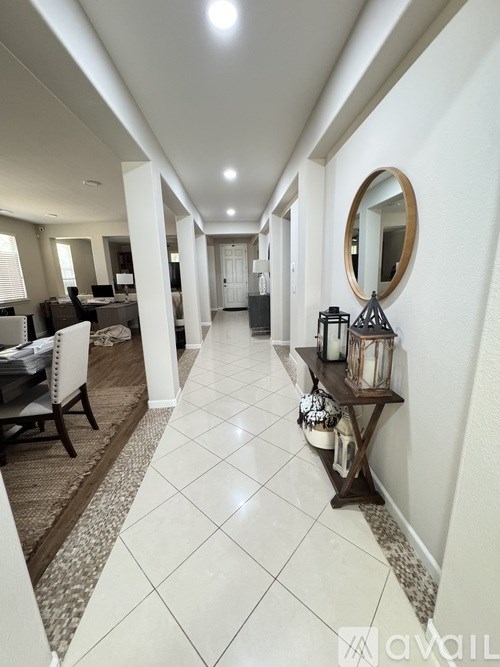 A long hallway with a table and chairs on the left and a mirror on the right.