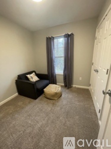 A room with a black chair and ottoman in front of a window with curtains.