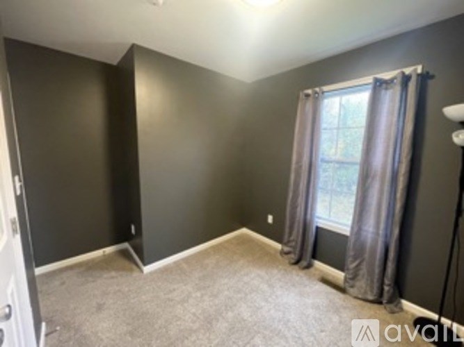 A room with grey carpet and a window with curtains.