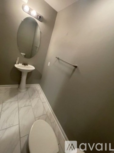 A bathroom with a toilet, sink, mirror, and a light on the wall.