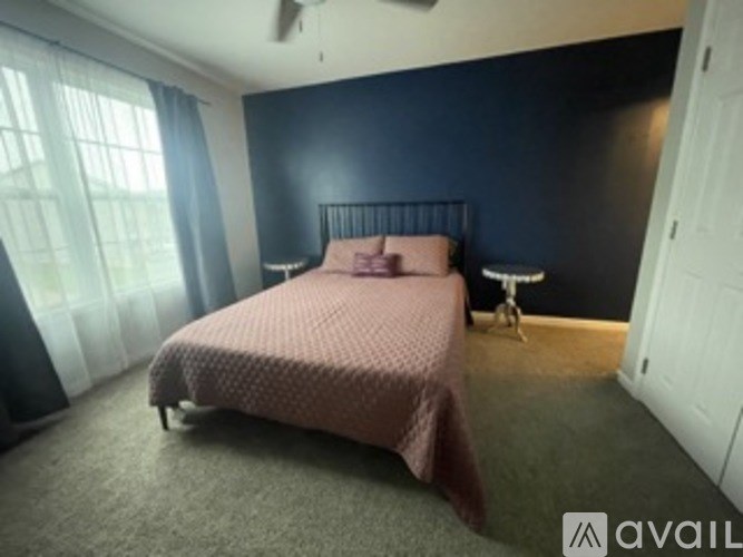 A bedroom with a bed, a small table, and a window with curtains.