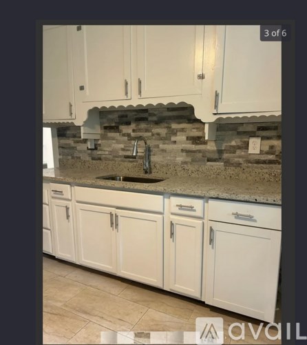 A kitchen with white cabinets and a stone backsplash.