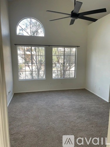 A room with a ceiling fan and two windows.