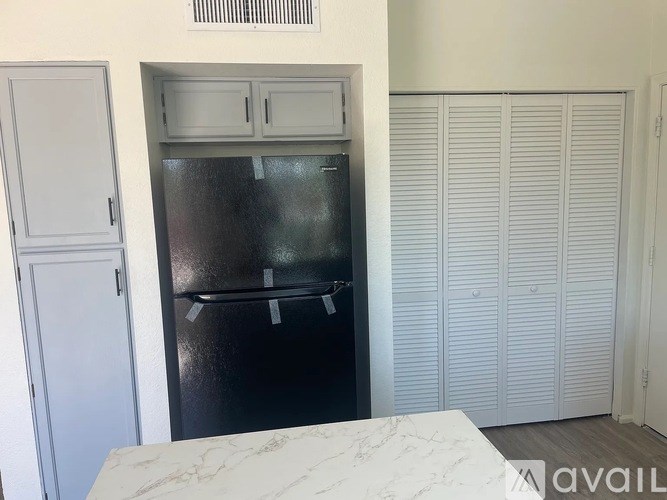 A black fridge in a kitchen with white cabinets and a marble countertop.