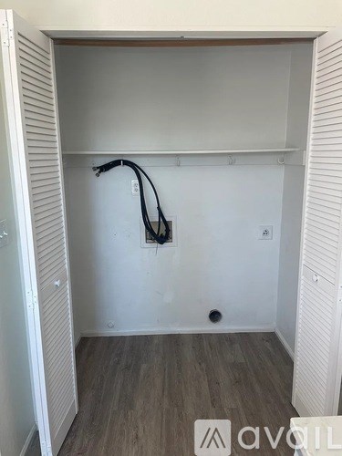 A room with a white wall and a wooden floor with a hose hanging on the wall.