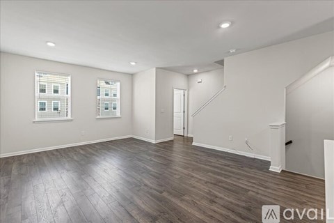 A spacious room with wooden flooring and a staircase in the background.