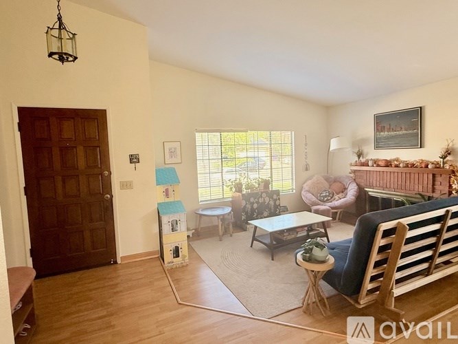 A living room with a brown door, a white wall, a window, a couch, a chair, a coffee table, and a rug.
