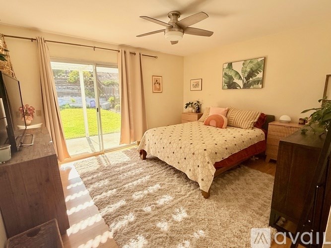 A bedroom with a bed, a ceiling fan, and a sliding glass door.
