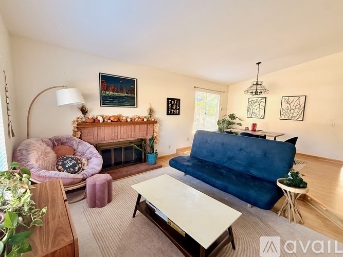 A living room with a blue couch, a pink chair, and a fireplace with a painting above it.